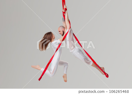 Beautiful girl and an athletic man in a white sport suits are performing an acrobatic elements in a studio. 106265468