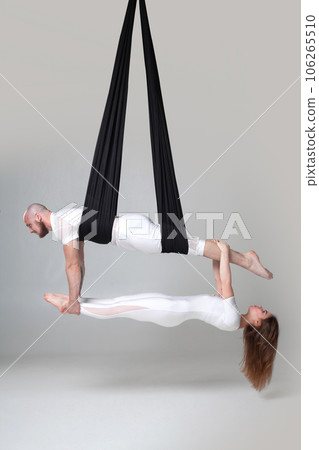 Beautiful girl and an athletic man in a white sport suits are performing an acrobatic elements in a studio. 106265510