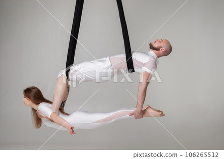 Beautiful girl and an athletic man in a white sport suits are performing an acrobatic elements in a studio. Beautiful girl and an athletic man in a white sport suits are performing an acrobatic elements in a studio. 106265512