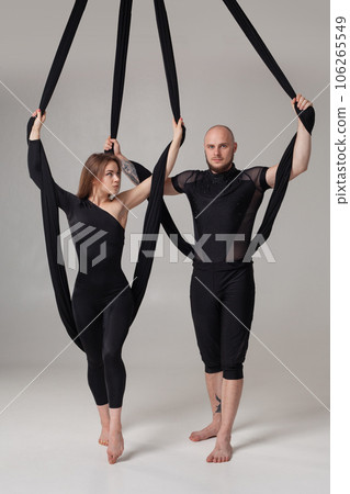 Beautiful girl and an athletic man in a black sport suits are performing an acrobatic elements in a studio. 106265549