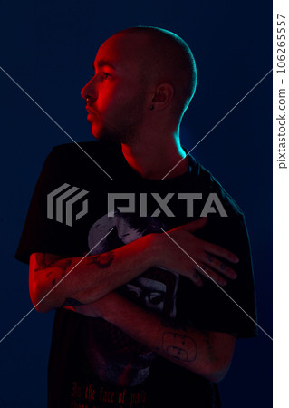 Studio shot of a young tattoed bald man posing against a blue background. 90s style. Studio shot of a young tattoed bald man posing against a blue background. 90s style. 106265557