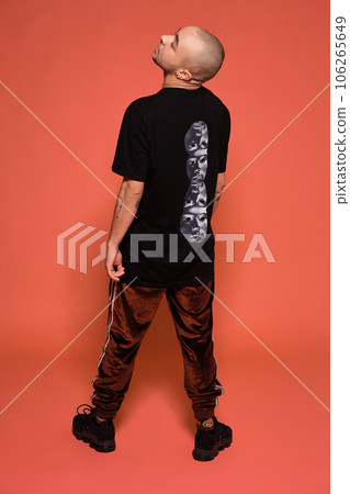 Studio shot of a young tattoed bald man posing against a pink background. 90s style. 106265649