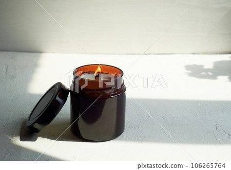 Candle in a glass of dark glass on a light background. The wooden wick is burning. Minimalism. Esotericism 106265764