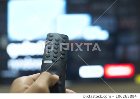 Hand with TV remote control, switching TV series from streaming service platform. The new way of enjoying entertainment at home. Hand with TV remote control, switching TV series from streaming service platform. The new way of enjoying entertainment at home. 106265894