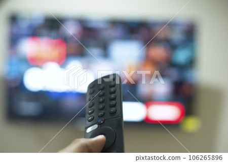 Hand with TV remote control, switching TV series from streaming service platform. The new way of enjoying entertainment at home. Hand with TV remote control, switching TV series from streaming service platform. The new way of enjoying entertainment at home. 106265896