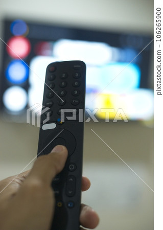 Hand with TV remote control, switching TV series from streaming service platform. The new way of enjoying entertainment at home. 106265900