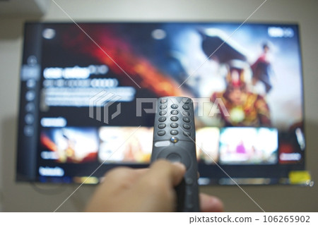Hand with TV remote control, switching TV series from streaming service platform. The new way of enjoying entertainment at home. Hand with TV remote control, switching TV series from streaming service platform. The new way of enjoying entertainment at home. 106265902