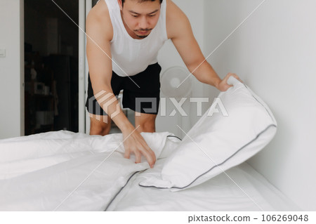 Man in white tank top is making bed folding into a sofa. 106269048