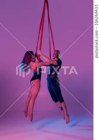 Beautiful girl and an athletic man in a black sport suits are performing an acrobatic elements in a studio. 106269433