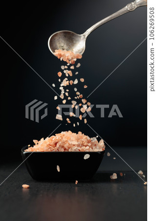 Pink salt is poured into a small black bowl. Pink salt is poured into a small black bowl. 106269508