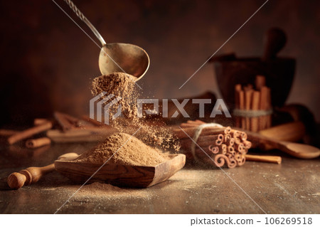 Cinnamon powder is poured into a wooden bowl. 106269518