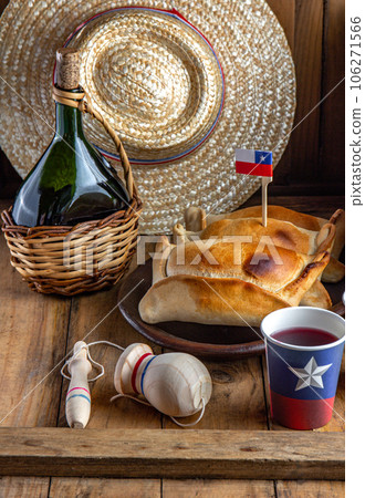 Chilean independence day concept. fiestas patrias. Tipical baked empanadas de pino, wine or chicha, hat and play emboque. Dish and drink on 18 September party, wooden background 106271566