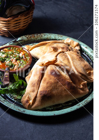 Tipical baked empanadas de pino with pebre sauce on vintage try, black stone background. Traditional chilean food for independence day party 106271574
