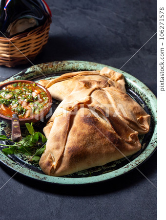 Tipical baked empanadas de pino with pebre sauce on vintage try, black stone background. Traditional chilean food for independence day party 106271578