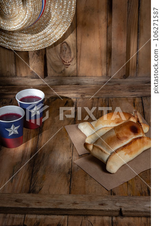 Chilean independence day concept. fiestas patrias. Tipical baked empanadas de pino, wine or chicha, hat and play emboque. Dish and drink on 18 September party, wooden background 106271587