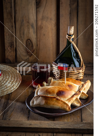 Chilean independence day concept. fiestas patrias. Tipical baked empanadas de pino, wine or chicha, hat and play emboque. Dish and drink on 18 September party, wooden background Chilean independence day concept. fiestas patrias. Tipical baked empanadas de pino, wine or chicha, hat and play emboque. Dish and drink on 18 September party, wooden background 106271592