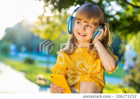 Happy child girl in wireless headphones choosing, listening music in smartphone dancing outdoors Happy child girl in wireless headphones choosing, listening music in smartphone dancing outdoors 106273252