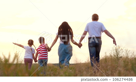 Family with little children plays plane and runs across meadow grass at sunset backside view. Children play with parents on family holiday at country. Family with children enjoys freedom at wilderness Family with little children plays plane and runs across meadow grass at sunset backside view. Children play with parents on family holiday at country. Family with children enjoys freedom at wilderness 106274486