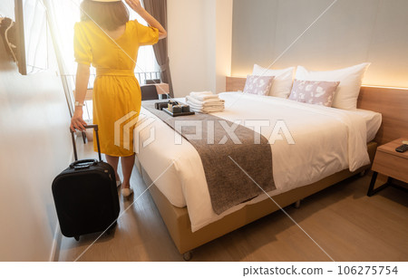 Tourist woman pulling her luggage in bedroom after arrival and check-in a hotel. Conceptual of comfortable accommodation while tourist travel during their holiday and vacation time. Tourist woman pulling her luggage in bedroom after arrival and check-in a hotel. Conceptual of comfortable accommodation while tourist travel during their holiday and vacation time. 106275754