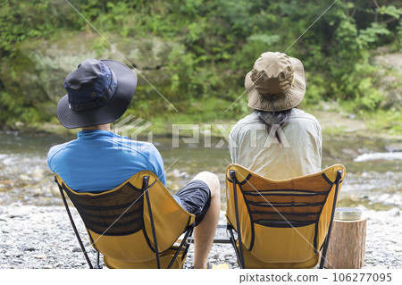 A young man and a woman sitting side by side on a chair and looking at the river A young man and a woman sitting side by side on a chair and looking at the river 106277095