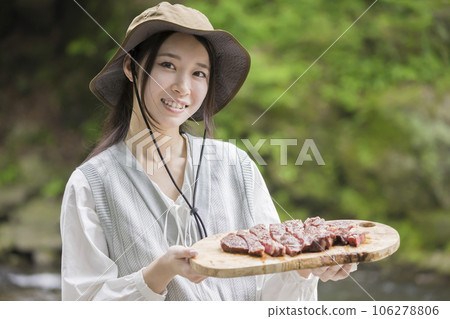 A woman putting barbecued steak meat on a cutting board A woman putting barbecued steak meat on a cutting board 106278806