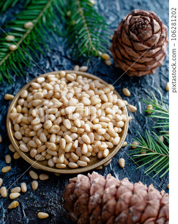 Shelled pine nuts in bowl. Still life of cedar kernels, fir cones and fir branches. Top view 106281202