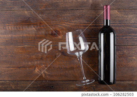 Bottle of red wine and an empty glass on a wooden background. 106282503