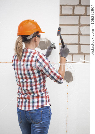 Insulation of the house with polyfoam. The worker is checking with the construction level the accuracy of the installation of polystyrene board on the facade. 106282904