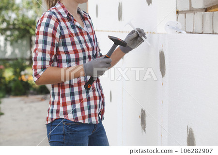 Insulation of the house with polyfoam. The worker is checking with the construction level the accuracy of the installation of polystyrene board on the facade. 106282907