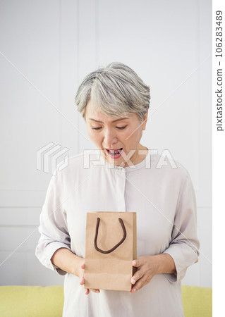 Portrait of an elderly Asian woman receives gift boxes, smiling and looking down while standing in a living room at home. Portrait of an elderly Asian woman receives gift boxes, smiling and looking down while standing in a living room at home. 106283489