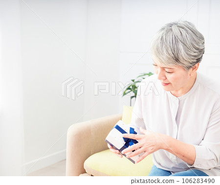 Portrait of an elderly Asian woman receives gift boxes, smiling and looking down in a living room at home. Portrait of an elderly Asian woman receives gift boxes, smiling and looking down in a living room at home. 106283490