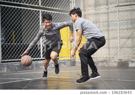 two young asian adult men playing one-on-one basketball on outdoor court two young asian adult men playing one-on-one basketball on outdoor court 106283643