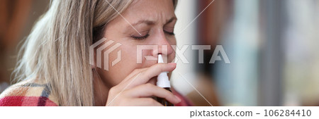 Woman with illness, covered in blanket, uses nasal spray close-up. Woman with illness, covered in blanket, uses nasal spray close-up. 106284410