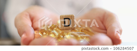 Human hands holding pile of vitamin D capsules with wooden cube with D symbol close up. Human hands holding pile of vitamin D capsules with wooden cube with D symbol close up. 106284507