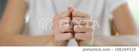 Woman sits at table with thick open book and holds her fists on book pages. 106284510