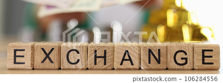 Wooden cubes with word exchange and blurred gold bars, coins and person with dollars in background Wooden cubes with word exchange and blurred gold bars, coins and person with dollars in background 106284556