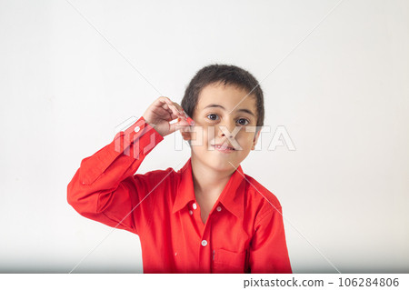 cute boy making a sly face. A cute looking boy in a red shirt making a slimy face in white room. Studio portrait, concept health with white background.   funny face. 106284806