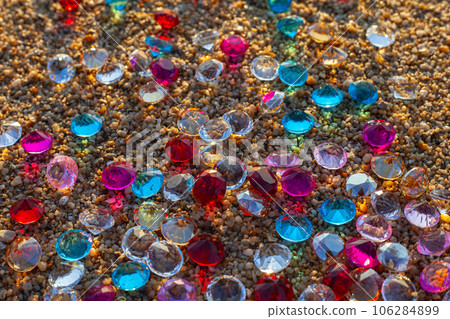 Colorful diamonds scattered on the beach The sun glistened off the facets of the precious stones,  creating a beautiful contrast with the white sand.colorful gemstones on the beach . 106284899