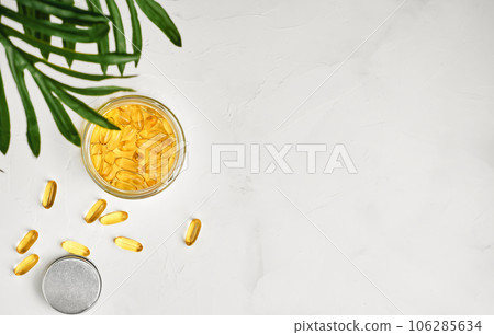 Fish oil capsules with omega 3 and vitamin D in a glass jar on a white concrete table top view, healthy eating concept. Selective focus. Cod liver oil softgels, layout with copy space Fish oil capsules with omega 3 and vitamin D in a glass jar on a white concrete table top view, healthy eating concept. Selective focus. Cod liver oil softgels, layout with copy space 106285634