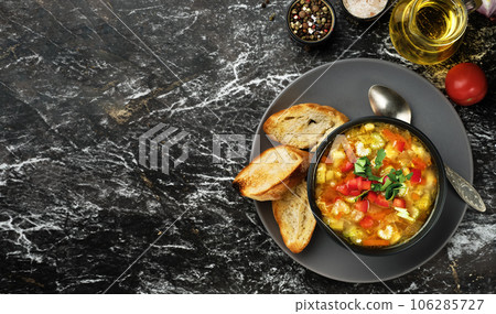 Minestrone soup in a black dish on a dark table, top view. Italian soup with seasonal vegetables. Delicious vegetarian food concept. Flat lay with copy space for text 106285727