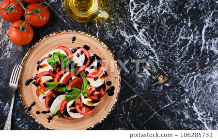 Tomatoes and mazzarella, Italian Caprese salad with tomatoes, mozzarella cheese, basil balsamic vinegar and olive oil. Dark marble background, top view, Vegetarian dish Tomatoes and mazzarella, Italian Caprese salad with tomatoes, mozzarella cheese, basil balsamic vinegar and olive oil. Dark marble background, top view, Vegetarian dish 106285731