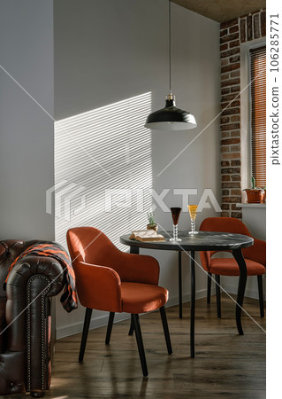 Stylish loft-style dining area with black wood table and red armchairs. Sunshine morning light from the window illuminates the dining area through the blinds. Retro style. 106285771