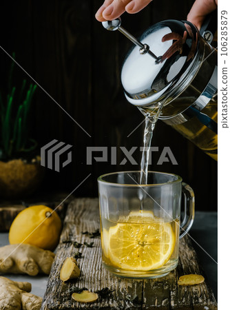 Ginger tea with lemon is poured into a glass from a teapot, close-up, ingredients for tea on a wooden vintage table. Prevention and support of immunity 106285879