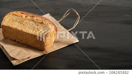 Loaf rustic bread on paper bag on black wooden table is prepared for delivery to buyer. Small business idea, baking and delivery of healthy natural sourdough bread to order. Top view with copy space Loaf rustic bread on paper bag on black wooden table is prepared for delivery to buyer. Small business idea, baking and delivery of healthy natural sourdough bread to order. Top view with copy space 106285882