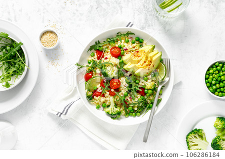 Couscous salad with broccoli, green peas, tomatoes, avocado and fresh arugula. Healthy natural plant based vegetarian food for lunch, israeli cuisine, top view Couscous salad with broccoli, green peas, tomatoes, avocado and fresh arugula. Healthy natural plant based vegetarian food for lunch, israeli cuisine, top view 106286184
