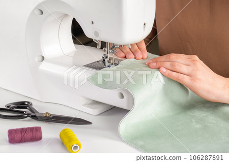Tailor hands stitching green fabric on modern sewing machine at workplace in atelier 106287891