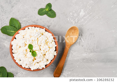 Homemade natural cottage cheese in a clay bowl, next to a wooden spoon, gray neutral background, layout with copy space. Soft curd natural healthy food, wholesome diet food 106289232