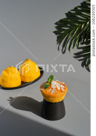 Delicious lemon muffin or cupcake with frosting and almond flakes. Homemade magdalena on gray neutral background, dish serving idea, close-up, selective focus 106289305