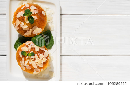Delicious lemon muffins or cupcake with icing and almond flakes. Homemade magdalena on white wooden background illuminated by sunlight, serving dish idea, top view with copy space. Delicious lemon muffins or cupcake with icing and almond flakes. Homemade magdalena on white wooden background illuminated by sunlight, serving dish idea, top view with copy space. 106289311