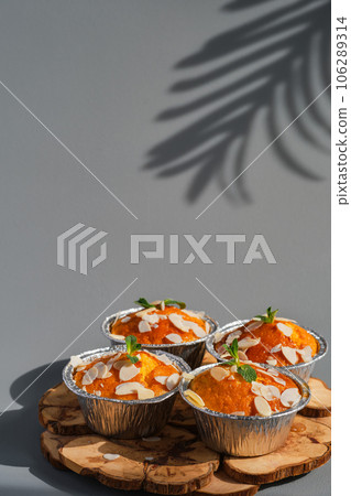 Delicious lemon muffins or cupcakes with frosting and almond flakes. Homemade magdalena on gray neutral background, dish serving idea, close-up, selective focus 106289314